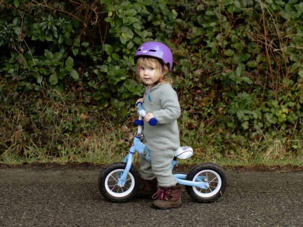 Bindungstypen sicher: Ein kleines Mädchen mit einem Laufrad schaut zum Erwachsenen, der das Bild vermutlich aufgenommen hat. Sicher gebundene Kinder können die Welt entdecken.
