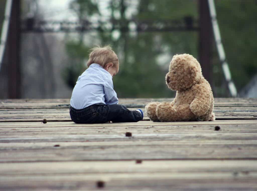 Bindungstypen unsicher-distanziert: Ein etwa dreijähriges Kind sitzt neben einem Teddy-Bär, der fast so groß ist wie es selbst. 